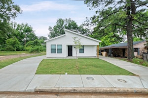Single-story white home with a new concrete driveway and a clean exterior. The property is currently secured with boarded windows and doors